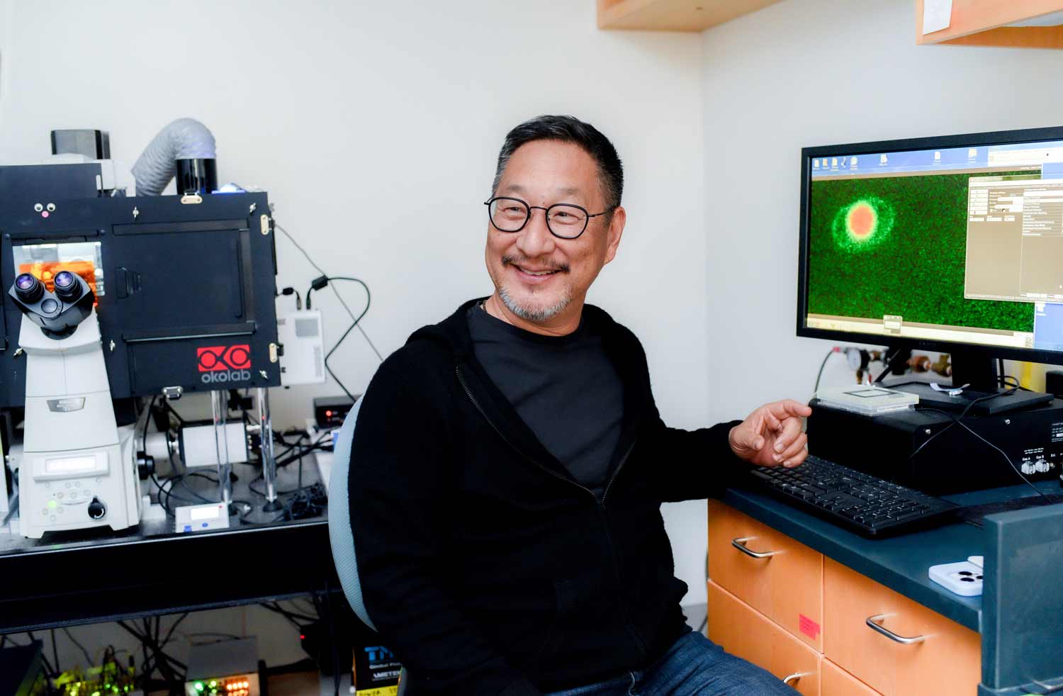 Fred Chang sits at desk, where a computer monitor displays a yeast cell with an oversized nucleus.