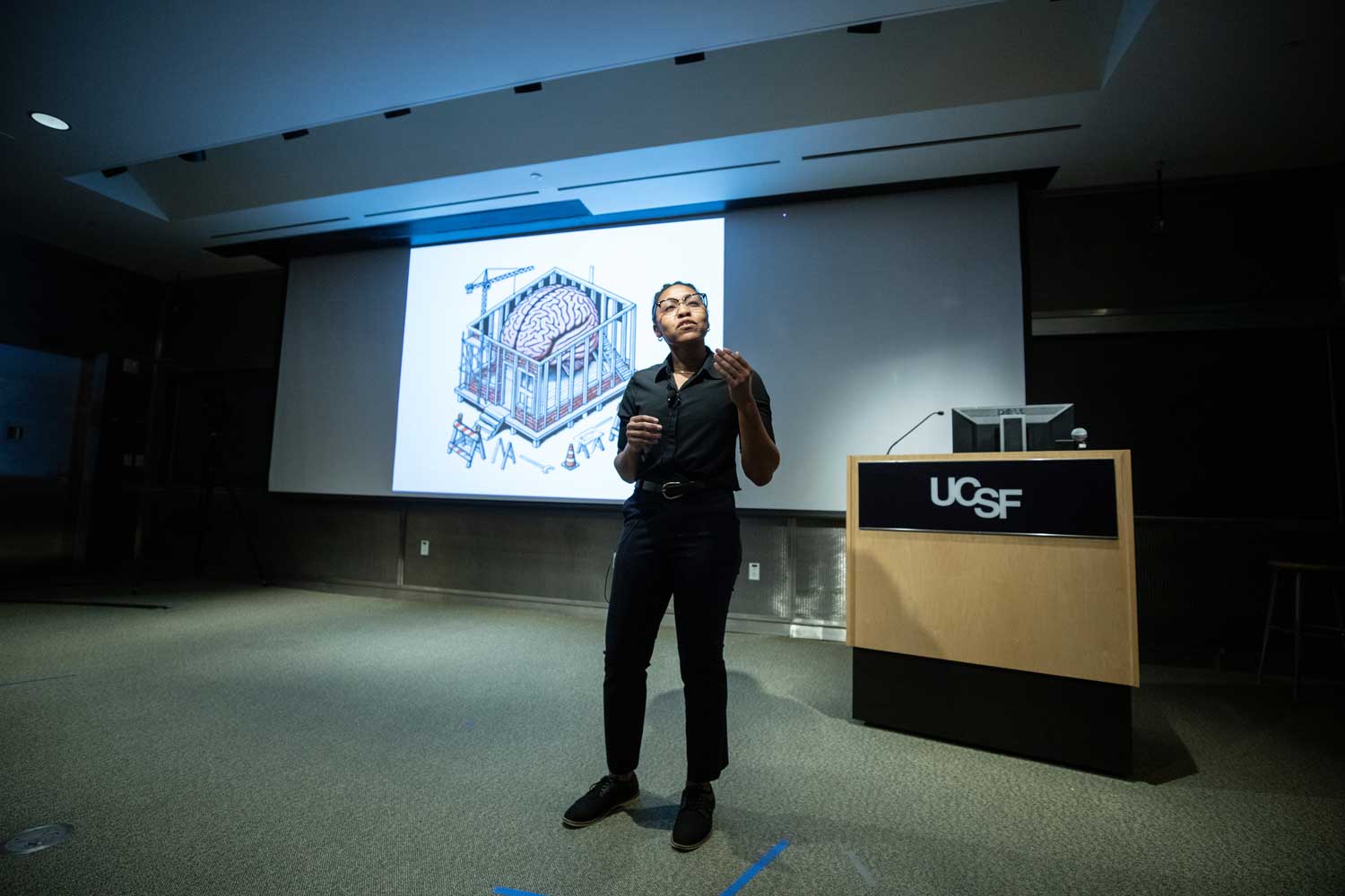Third place winner Kaylee Wedderburn-Pugh delivers her talk onstage, with a projection screen showing a brain.