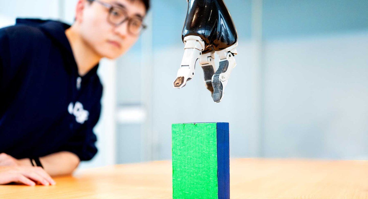 Graduate student Runfeng Miao watches a robotic arm move downward to grab a block.
