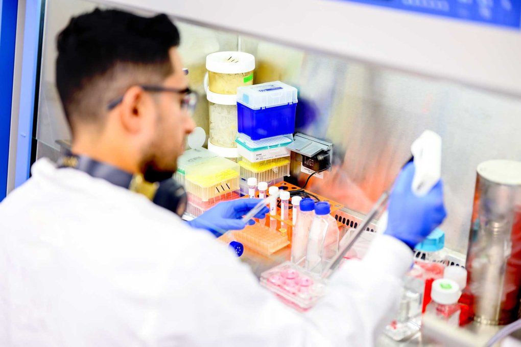 A postdoctoral student named Oscar Campos wears a lab coat as he conducts scientific research in a lab.