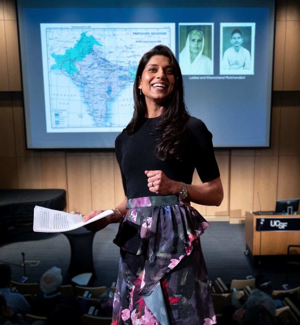 Rupa smiles at audience with old family images behind her on screen